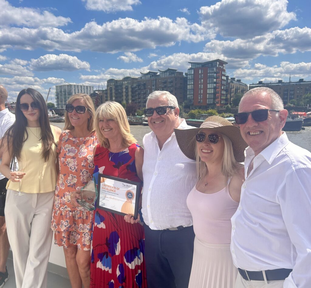 Helen standing outside with CleanTEC colleagues, smiling and holding her Cleaning Operative of the Year award.