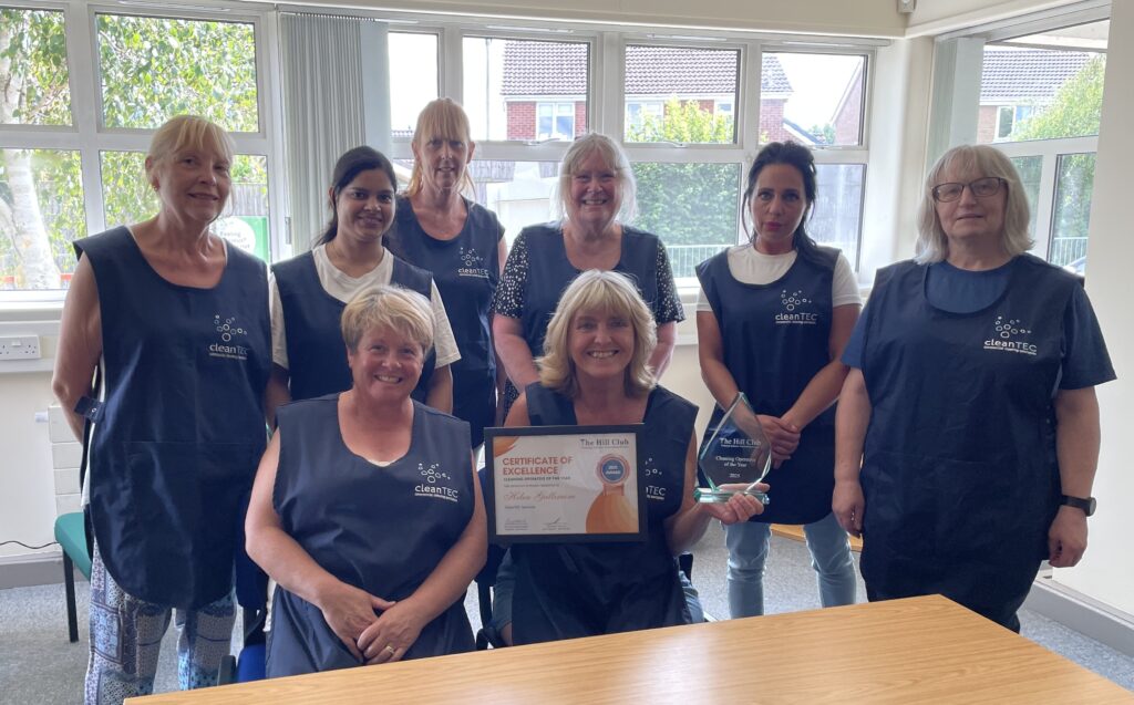 Helen with CleanTEC colleagues, smiling and holding her Cleaning Operative of the Year award.